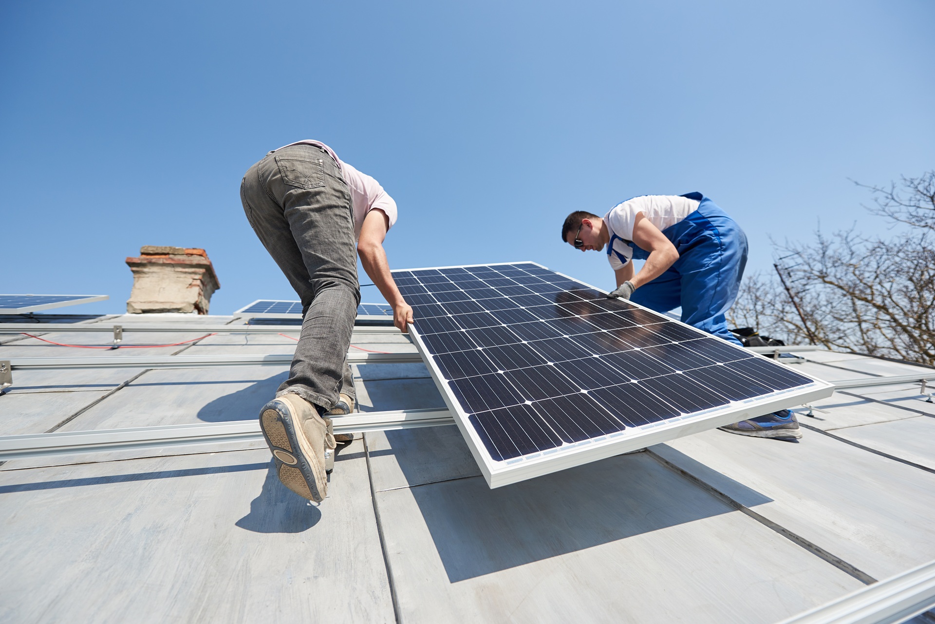 Zwei Techniker montieren Solarpanels auf einem Hausdach bei Sonnenschein | Fronius Hybrid Wechselrichter