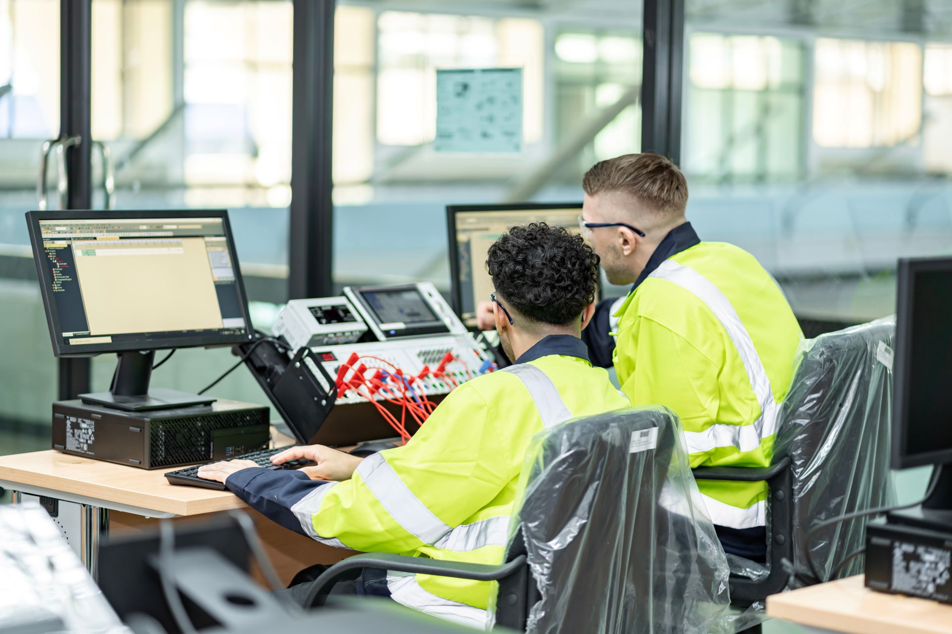 Zwei Mitarbeitende prüfen eine verdrahtete Testeinheit in einem industriellen Arbeitsplatz – Qualitätssicherung bei der Kabelkonfektionierung